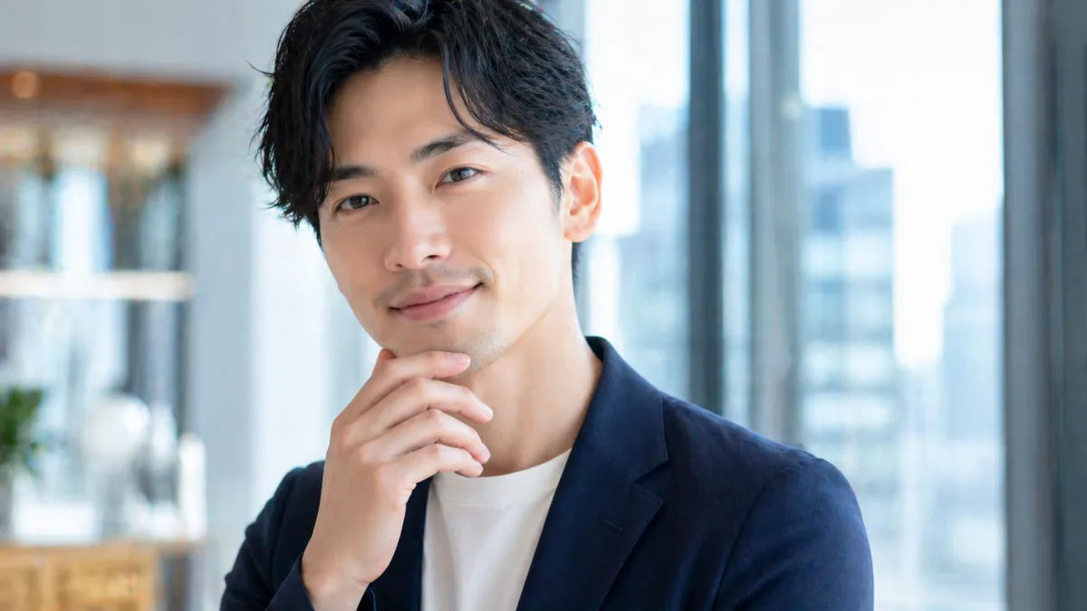 清潔感のある20代～30代日本人男性が都会的な背景の前で爽やかな表情を見せる、男性美容をイメージしたファーストビュー向け写真
